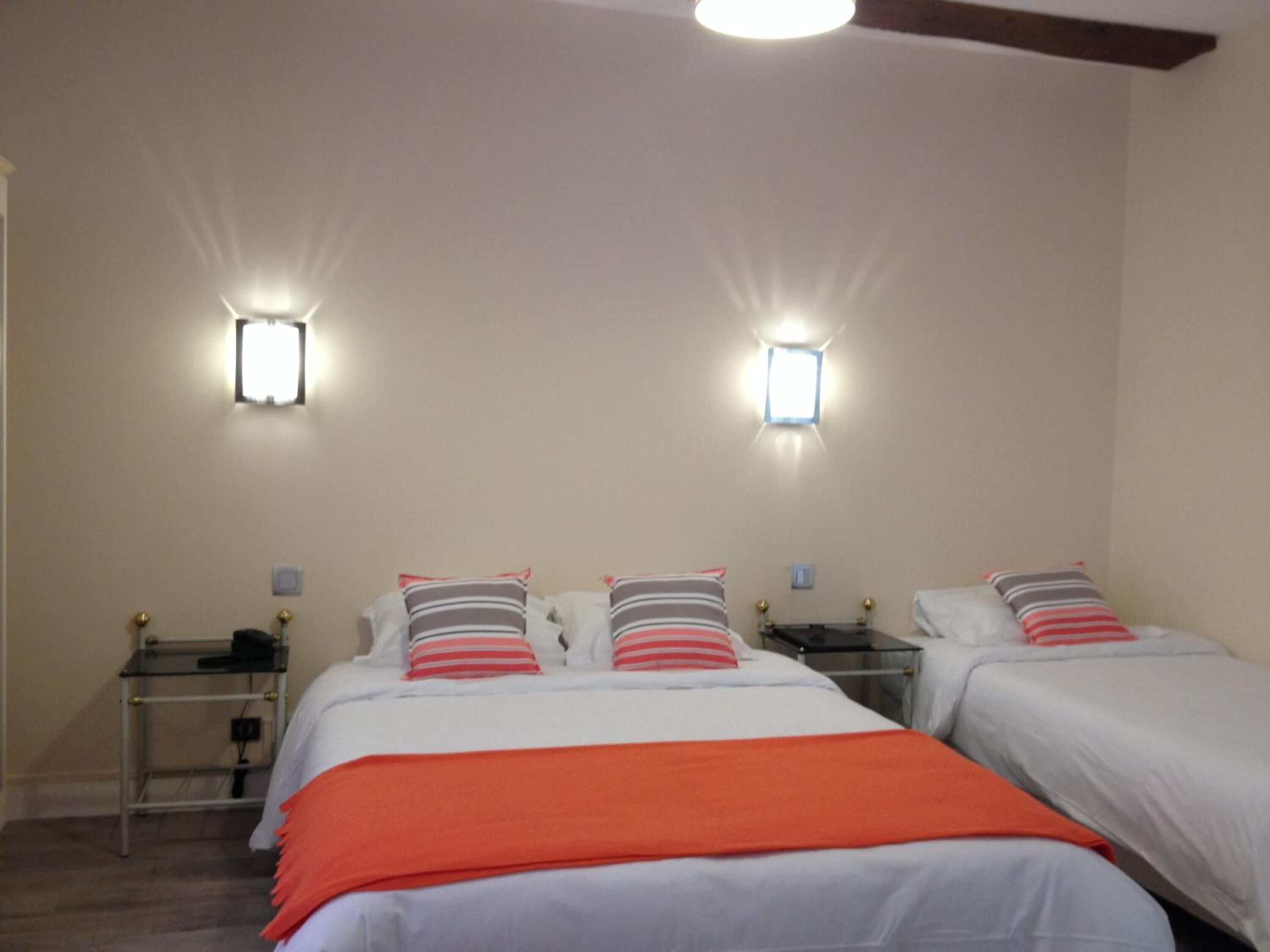 A hotel room with two beds, each with white bedding and striped pillows. There are two bedside tables with lamps, and the room has a modern design with a ceiling light fixture.