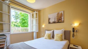 A bedroom with a bed, bedside table, and a window with a view of trees. - Hôtel Val De Loire (Azay-le-Rideau)