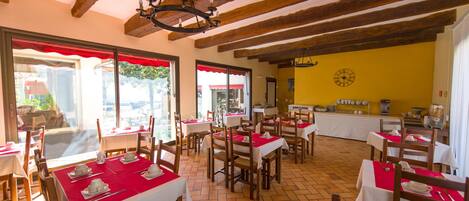 Un restaurant avec des poutres en bois, des nappes rouges et une horloge au mur.