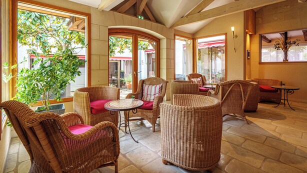 A spacious indoor area with wicker furniture, large windows, and a stone floor. - Hôtel Val De Loire (Azay-le-Rideau)