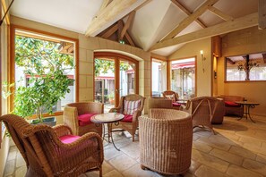 A spacious indoor area with wicker furniture, large windows, and a stone floor. - Hôtel Val De Loire (Azay-le-Rideau)