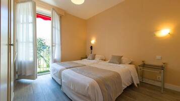 A bedroom with two beds, a glass bedside table, a nightstand, and a window with curtains.