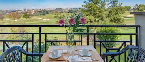 A table set for two with a view of a golf course and distant town.