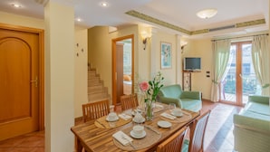 Uma sala de jantar com uma mesa de madeira posta para quatro pessoas, um vaso com flores e uma escada que leva a um andar superior.