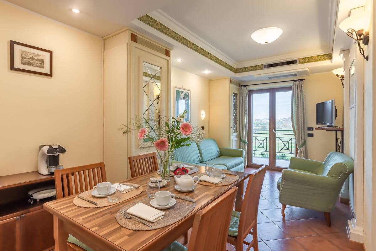 A dining area with a wooden table set for four, a coffee machine, and a vase with flowers.