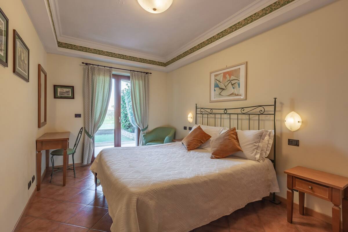 A bedroom with a bed, a chair, a desk, and a window with curtains.