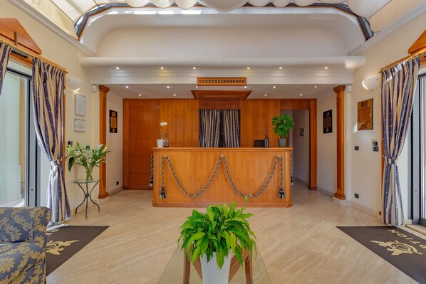 A hotel reception area with a wooden reception desk, potted plants, and a modern interior design.