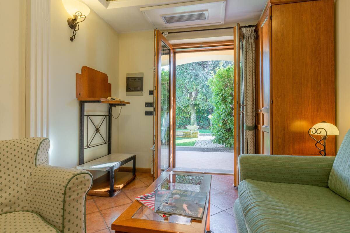 A room with a sofa, a coffee table with magazines, a side table, and a door leading to a garden.