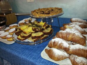A buffet table with various pastries and desserts, including a pie, muffins, and croissants. - Hotel La Plage (Cattolica)