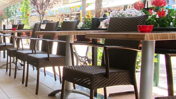 Un café al aire libre con sillas y mesas de mimbre, piso de baldosas y vista a la calle.