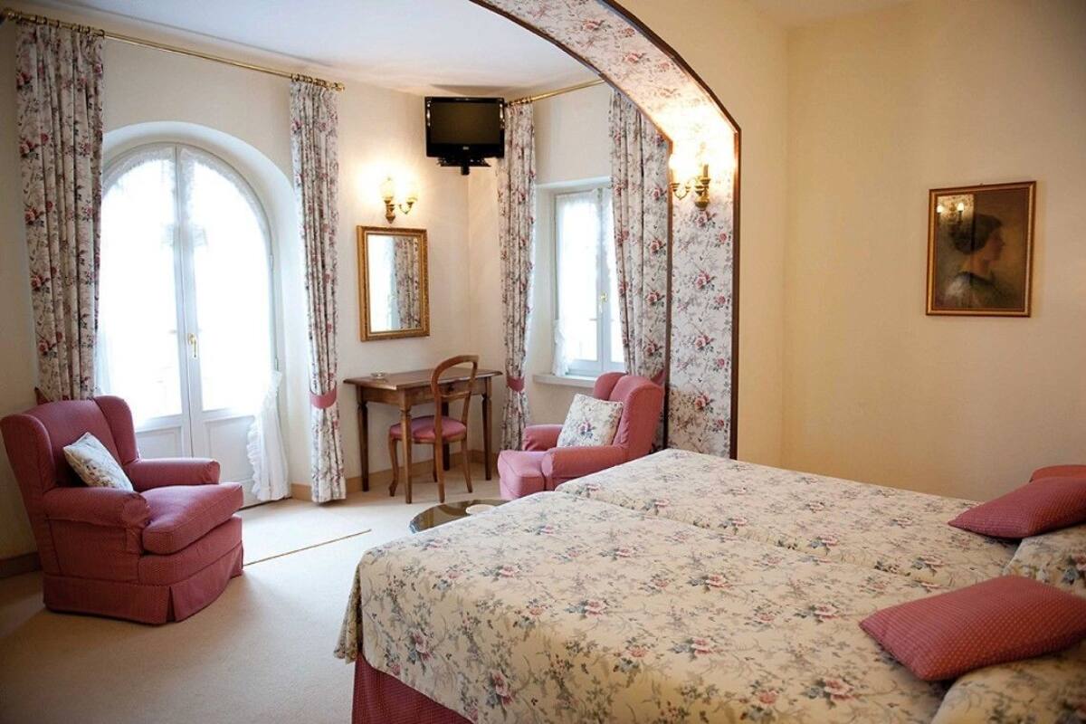 A bedroom with a large bed, a desk, a chair, and a television.