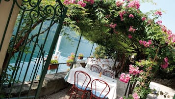An outdoor dining area with tables and chairs, surrounded by greenery and overlooking a body of water.