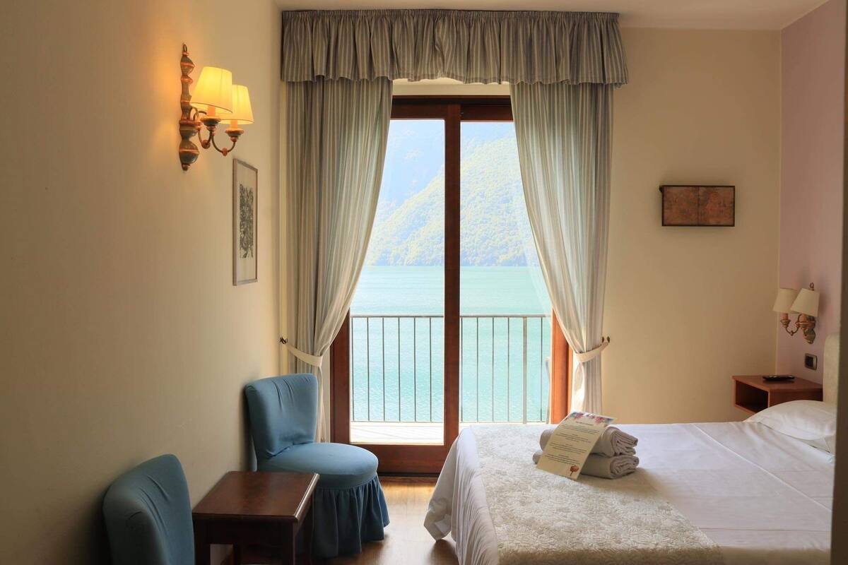 A hotel room with a bed, a chair, a table, and a view of the sea through large windows.
