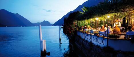 A waterfront restaurant with outdoor seating, a view of the lake, and a sign reading "HOTEL STELLA DITALIA".