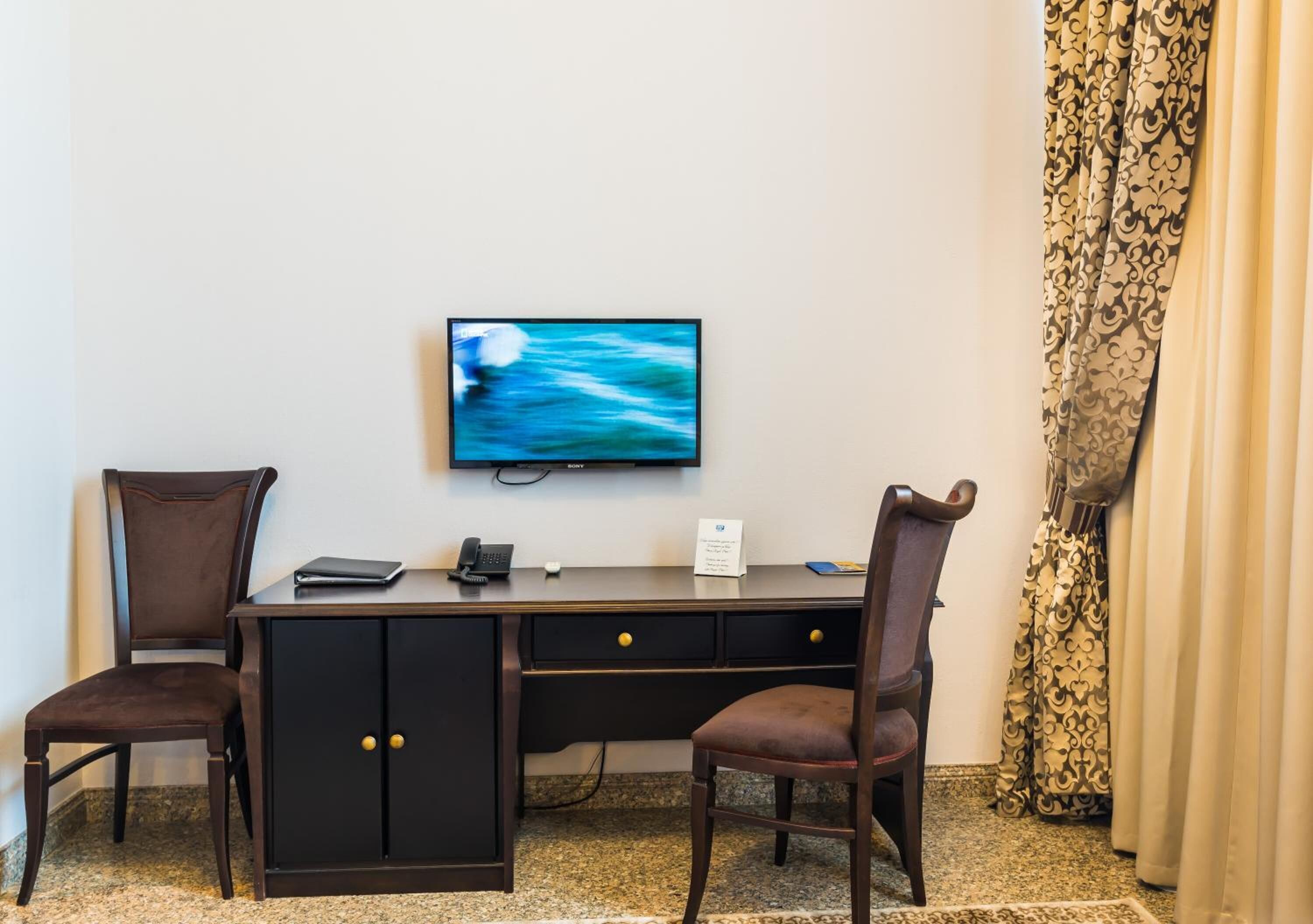 A hotel room with a desk, two chairs, a television, and a patterned curtain.
