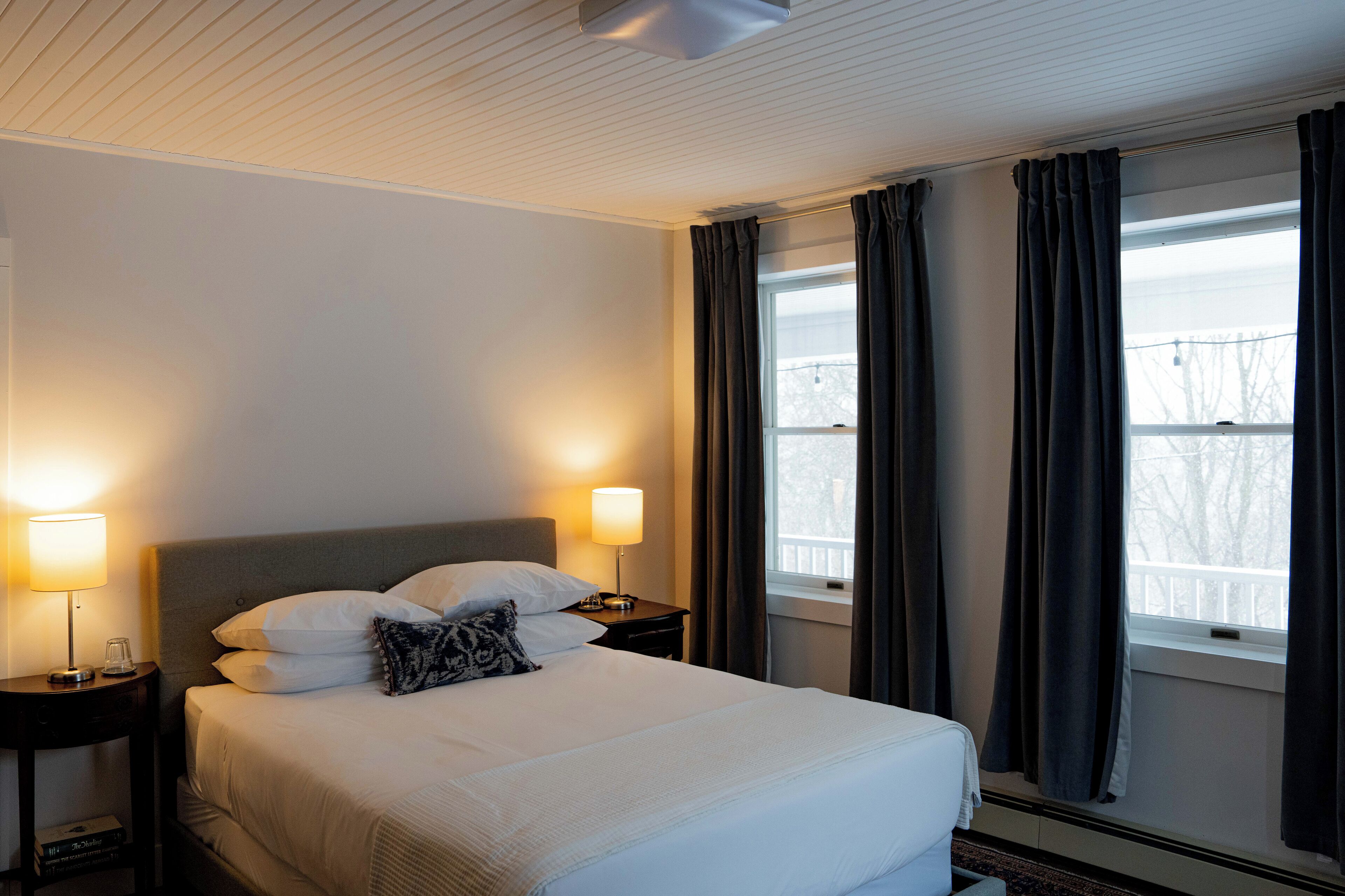 A hotel room with a large bed, two bedside lamps, a nightstand, and a window with curtains.