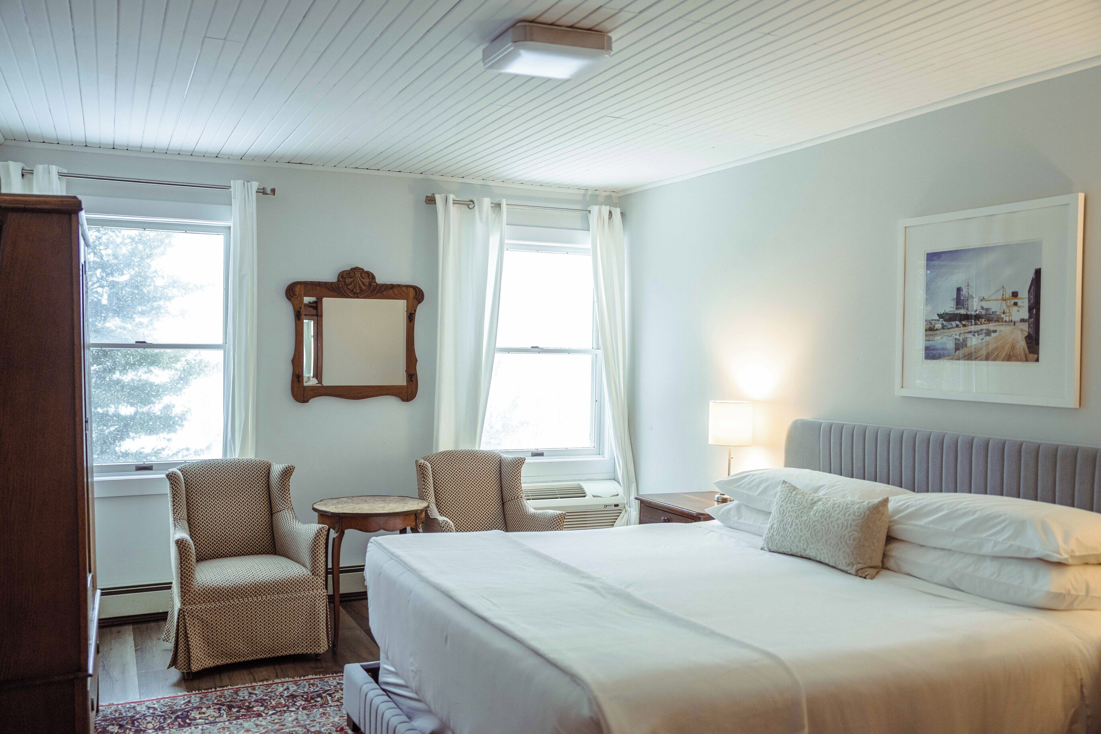 Habitación de hotel con una cama, dos sillas, una mesita, un espejo y un cuadro en la pared.