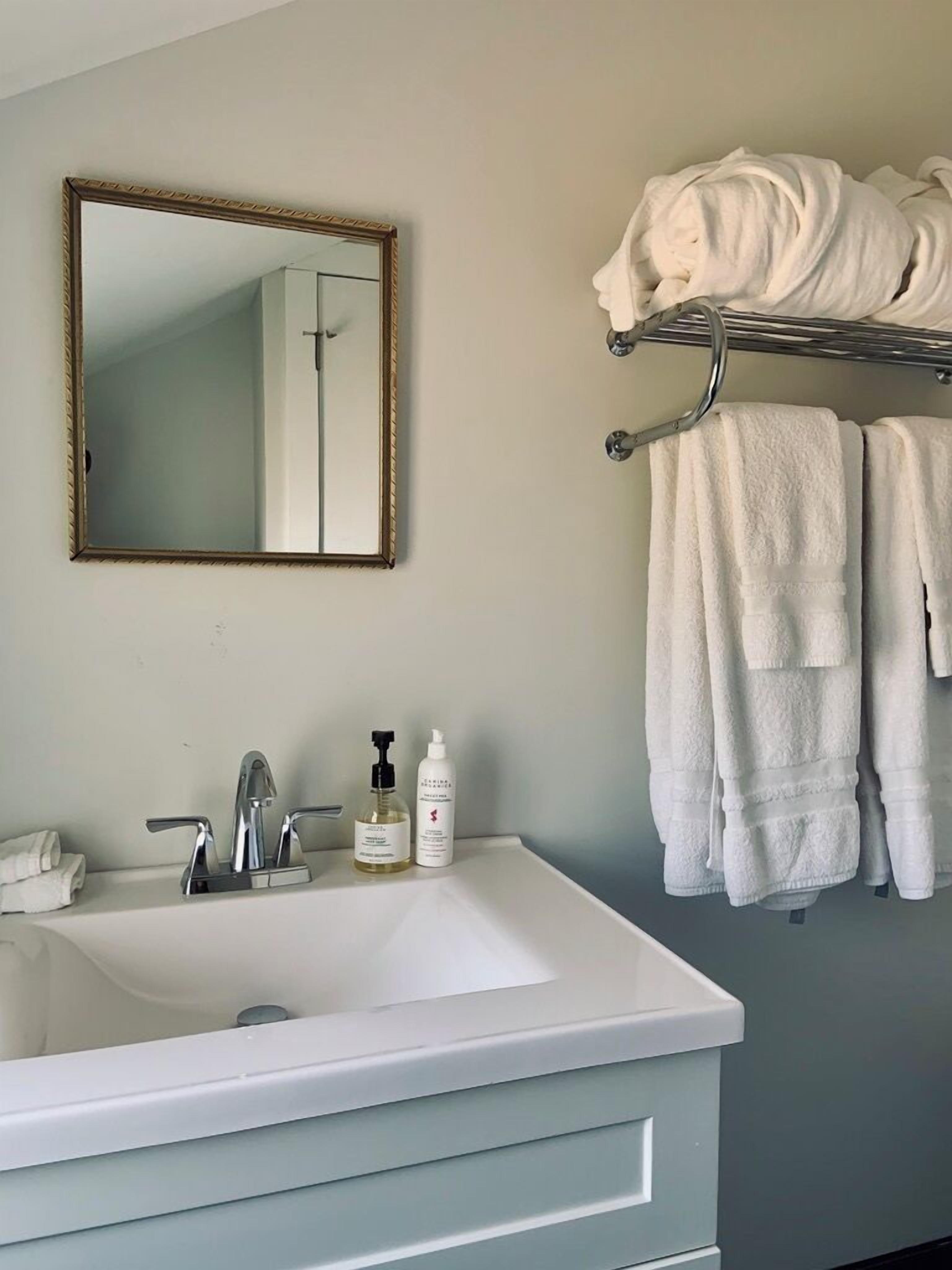 Une salle de bain avec un lavabo blanc, un miroir et un porte-serviettes sur lequel sont pliées des serviettes.