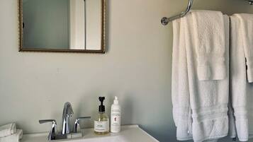 Une salle de bain avec un lavabo blanc, un miroir et un porte-serviettes sur lequel sont pliées des serviettes.