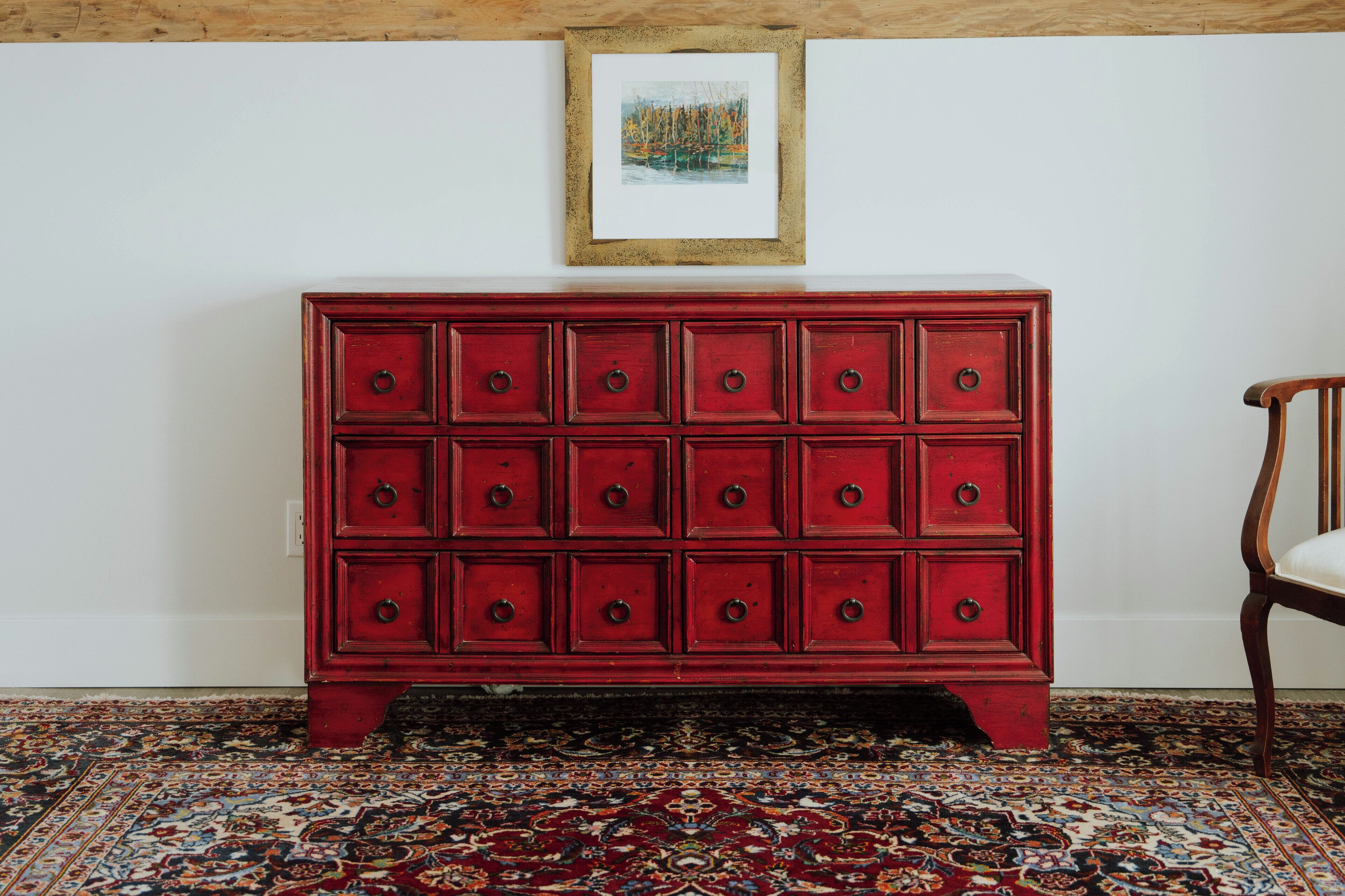 Ein roter Schminktisch mit mehreren Schubladen, ein gerahmtes Bild an der Wand und ein gemustertes Teppich.
