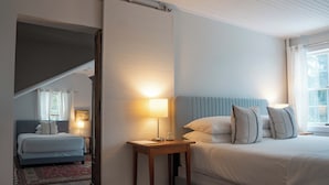 Un dormitorio con una cama grande, una mesita de noche con lámpara y vistas a una escalera que conduce a otra habitación.