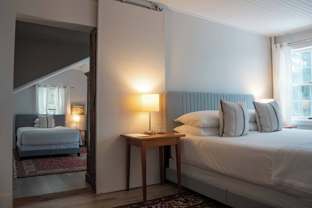 Une chambre avec un grand lit, une table de chevet avec une lampe, et une vue sur un escalier menant à une autre pièce.