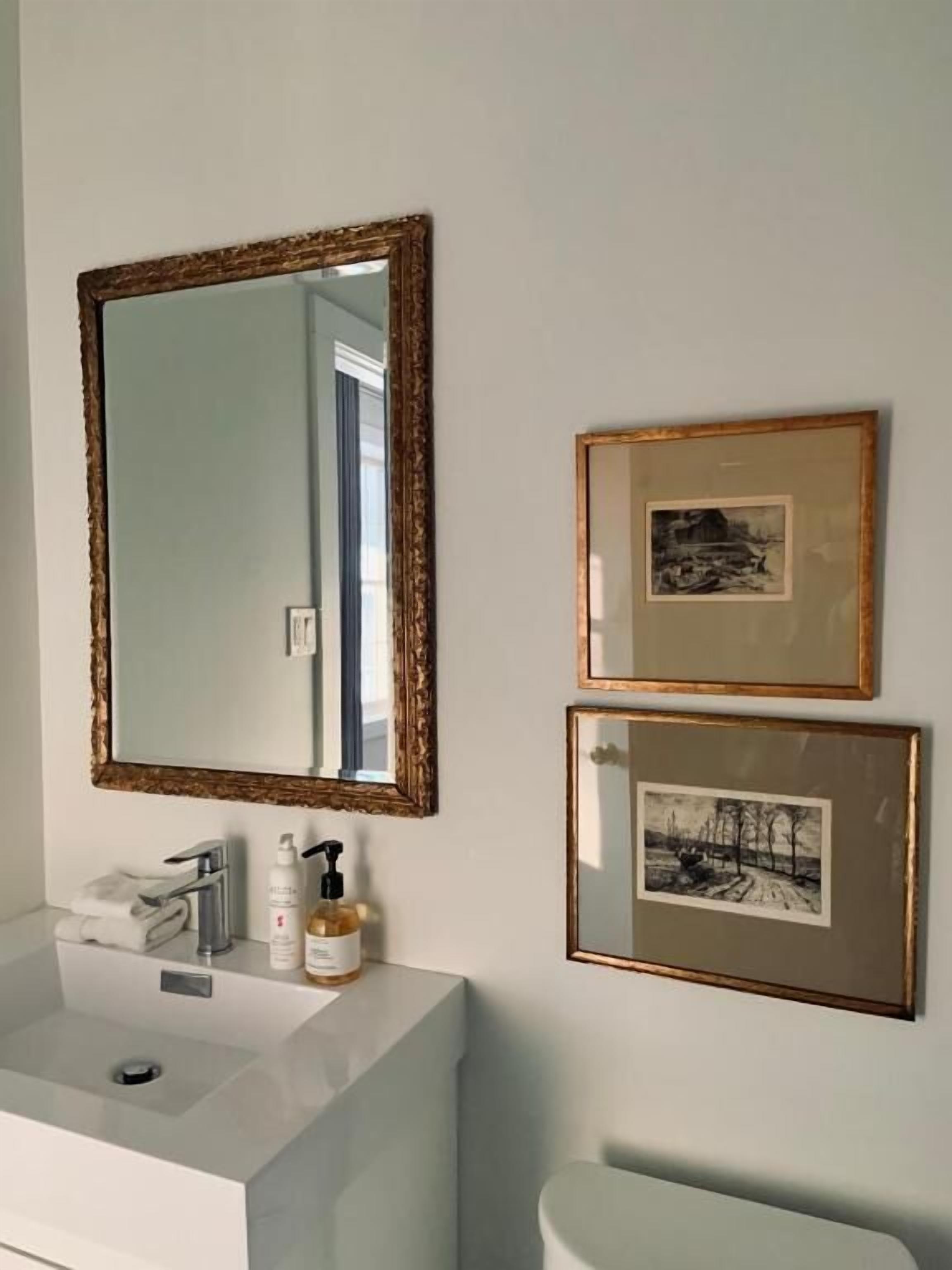 A bathroom with a large mirror, a sink, and two framed pictures on the wall.