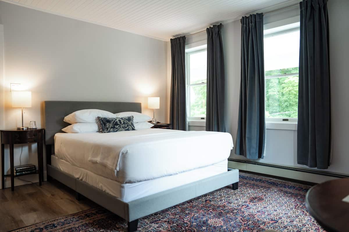 Une chambre à coucher bien rangée, avec un grand lit, deux lampes de chevet, une table de nuit et une fenêtre avec des rideaux.