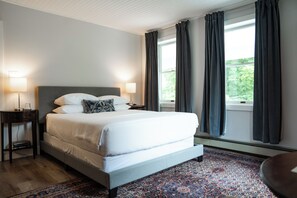 Une chambre à coucher bien rangée, avec un grand lit, deux lampes de chevet, une table de nuit et une fenêtre avec des rideaux.