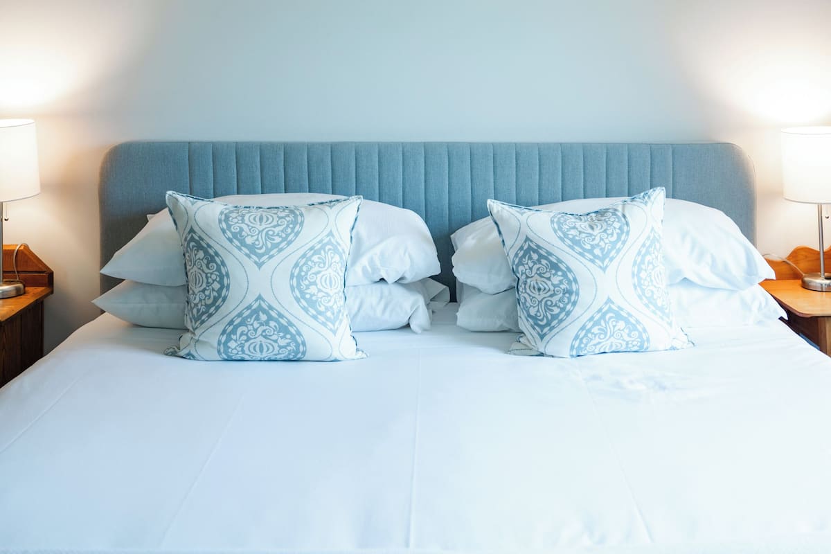 Un lit bien fait, avec une tête de lit bleue, du linge de lit blanc et des coussins à motifs.