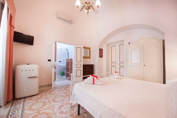 A hotel room with a bed, a television mounted on the wall, a refrigerator, and a bathroom visible through an open door. - Agriturismo Villantica (Tuglie)