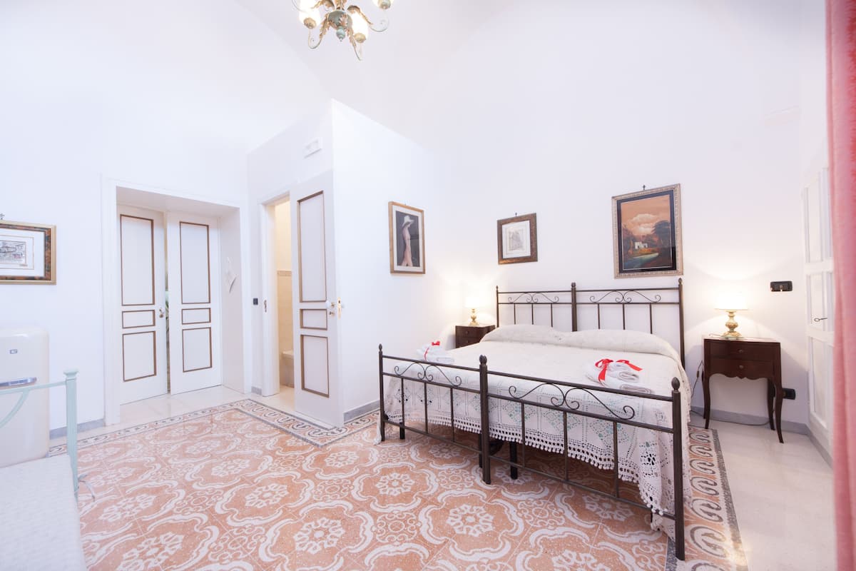 Ein Schlafzimmer mit Bett, Nachttisch, Stuhl, einer Tür und einer Wand mit gerahmten Bildern.