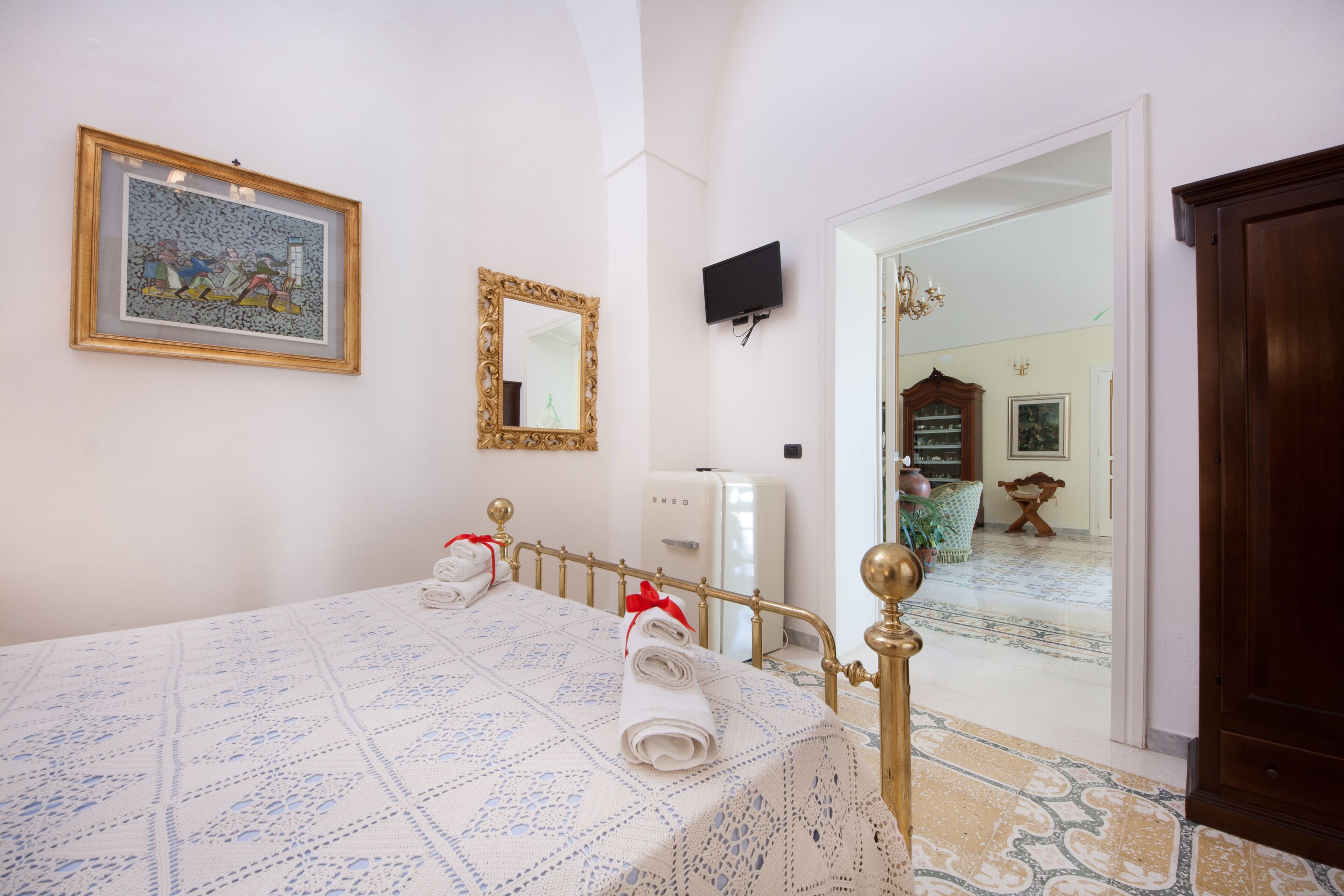 Una camera d'albergo con un letto, una televisione, uno specchio e una porta che dà su un'altra stanza.
