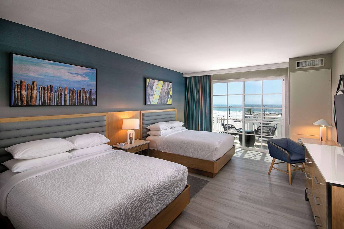 A hotel room with two beds, a desk, and a view of the ocean.