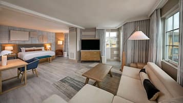 A modern hotel room with a large bed, a TV, a sofa, a coffee table, and a desk with a lamp.