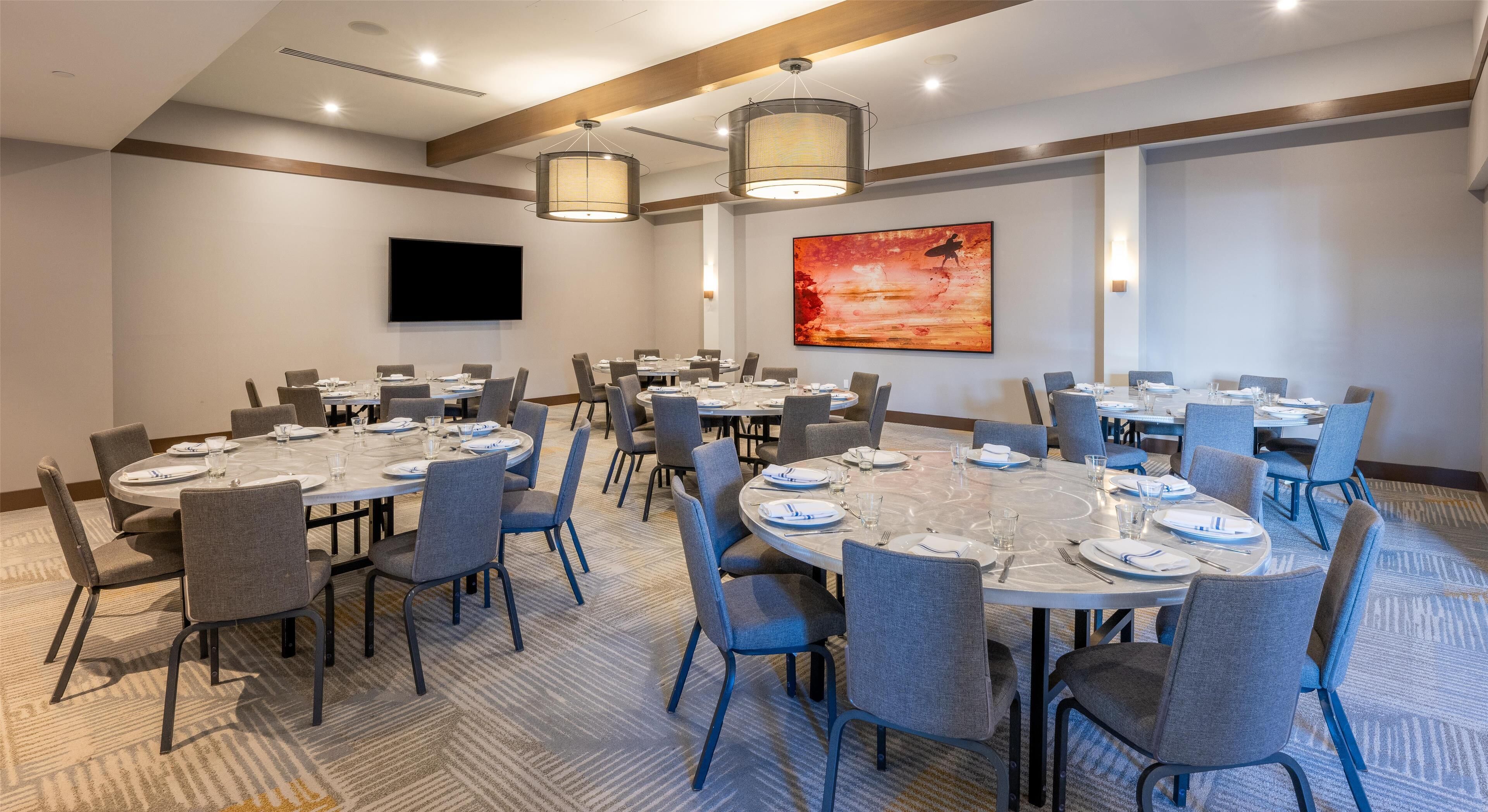 A conference room with round tables, grey chairs, and a flat-screen TV on the wall.