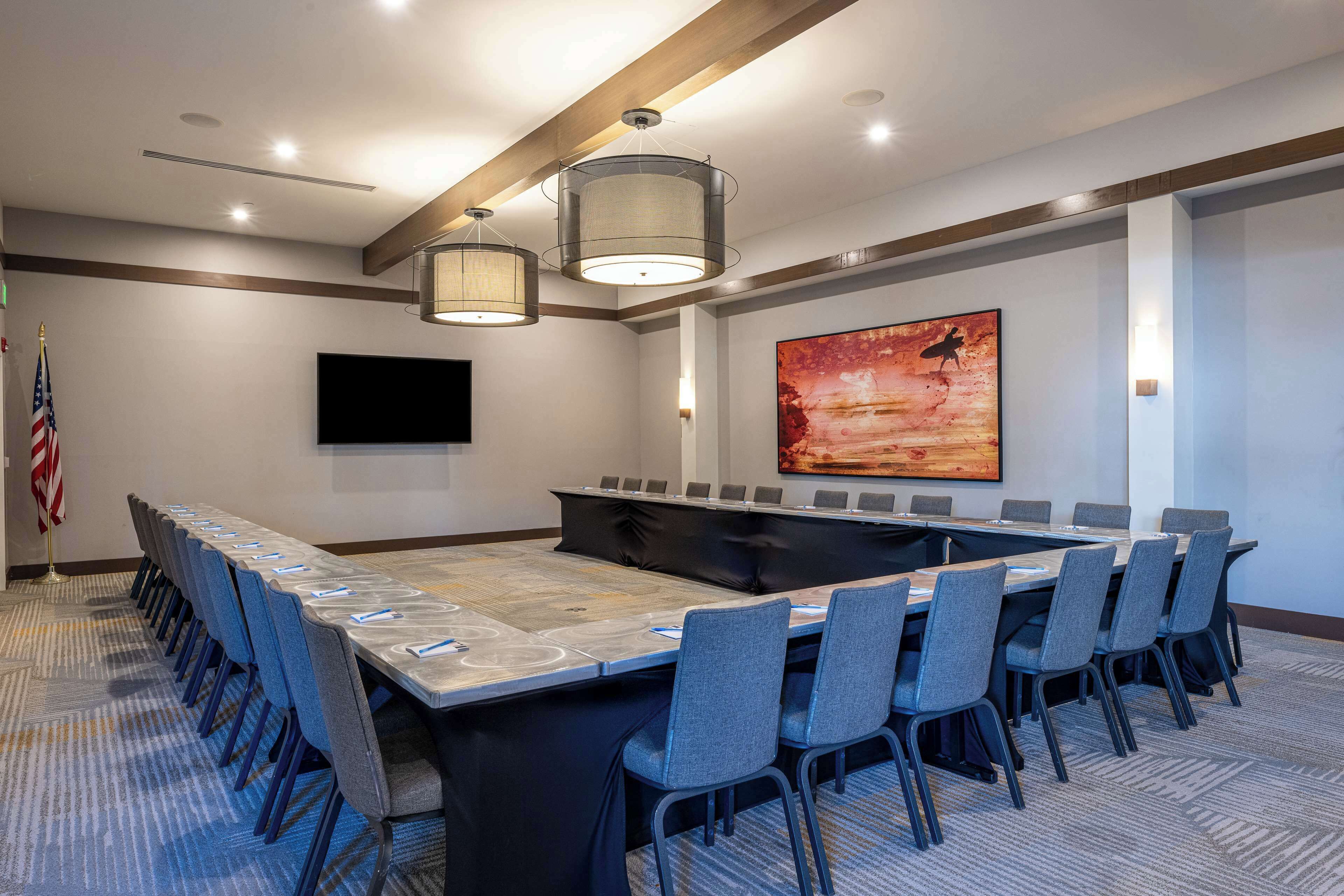 A conference room with a long table, chairs, a flag, and a painting on the wall.