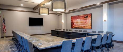 A conference room with a long table, chairs, a flag, and a painting on the wall.
