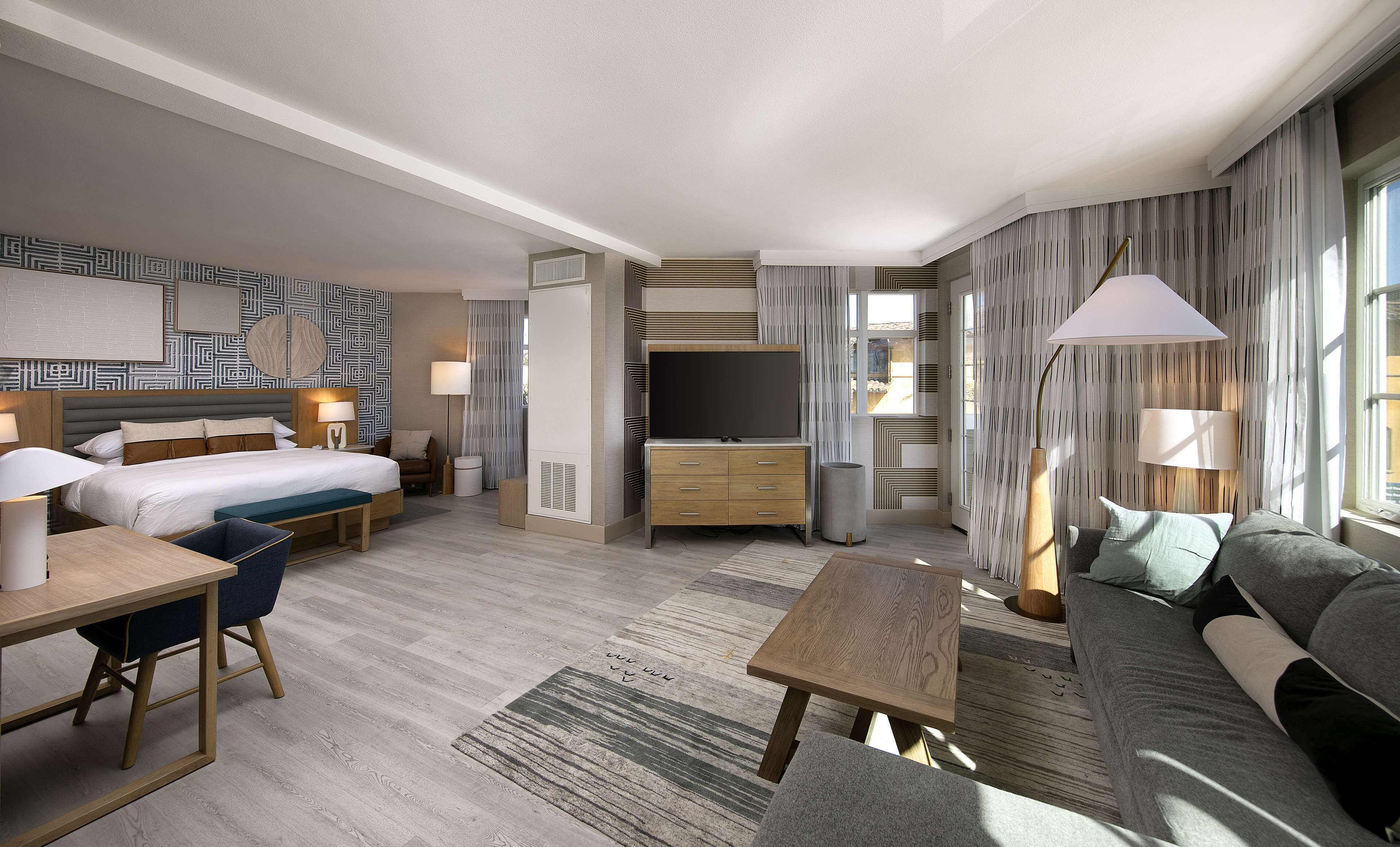 A modern hotel room with a bed, desk, sofa, and TV.