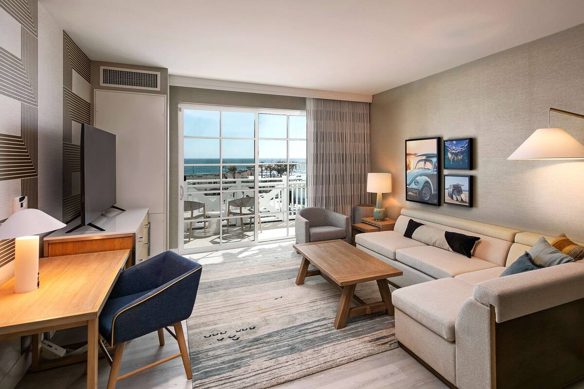 A modern hotel room with a balcony, a sofa, a desk, and a TV.