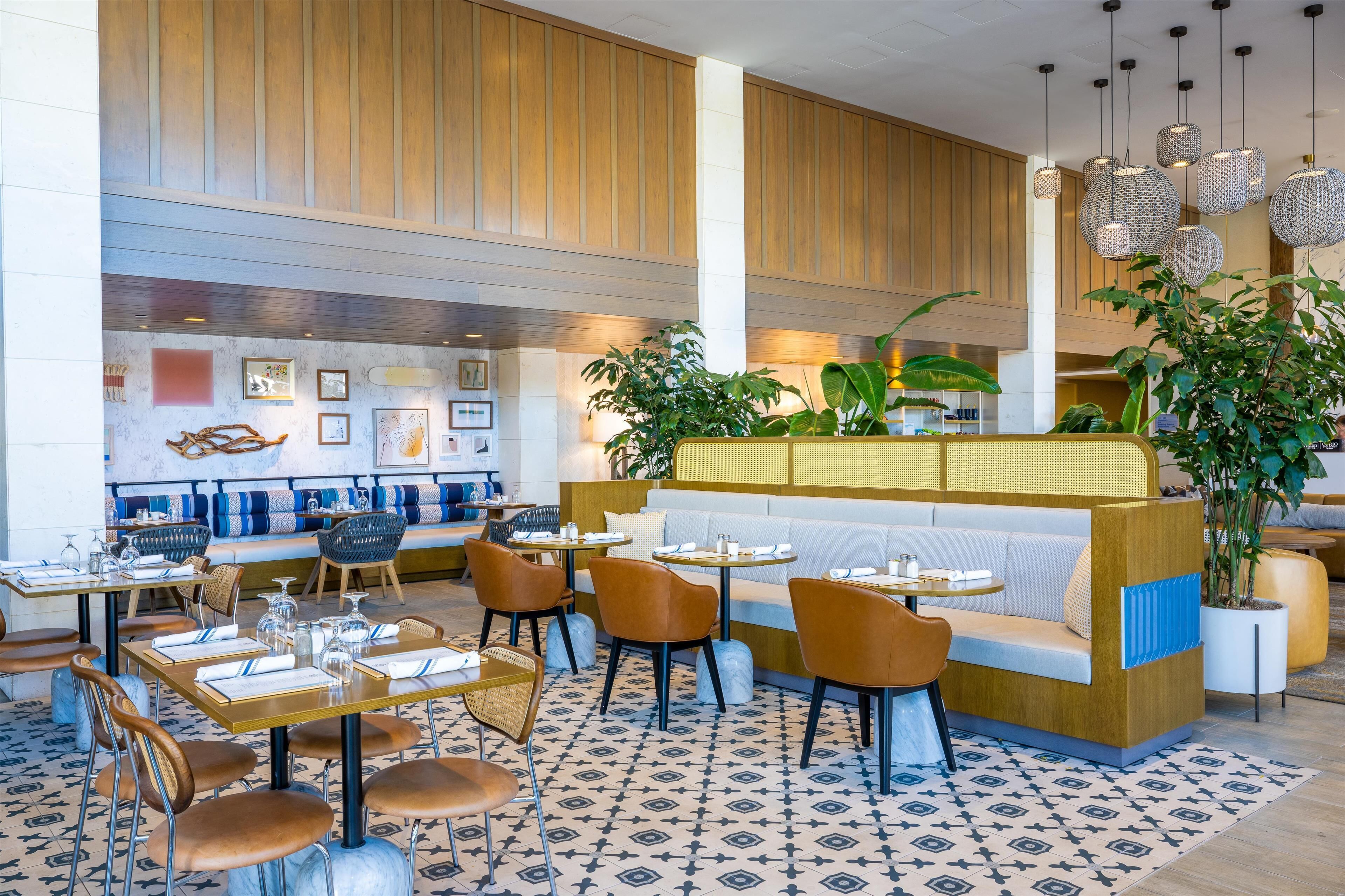 A modern restaurant with wooden panel walls, a central seating area with a white and blue cushioned bench, and a patterned floor.