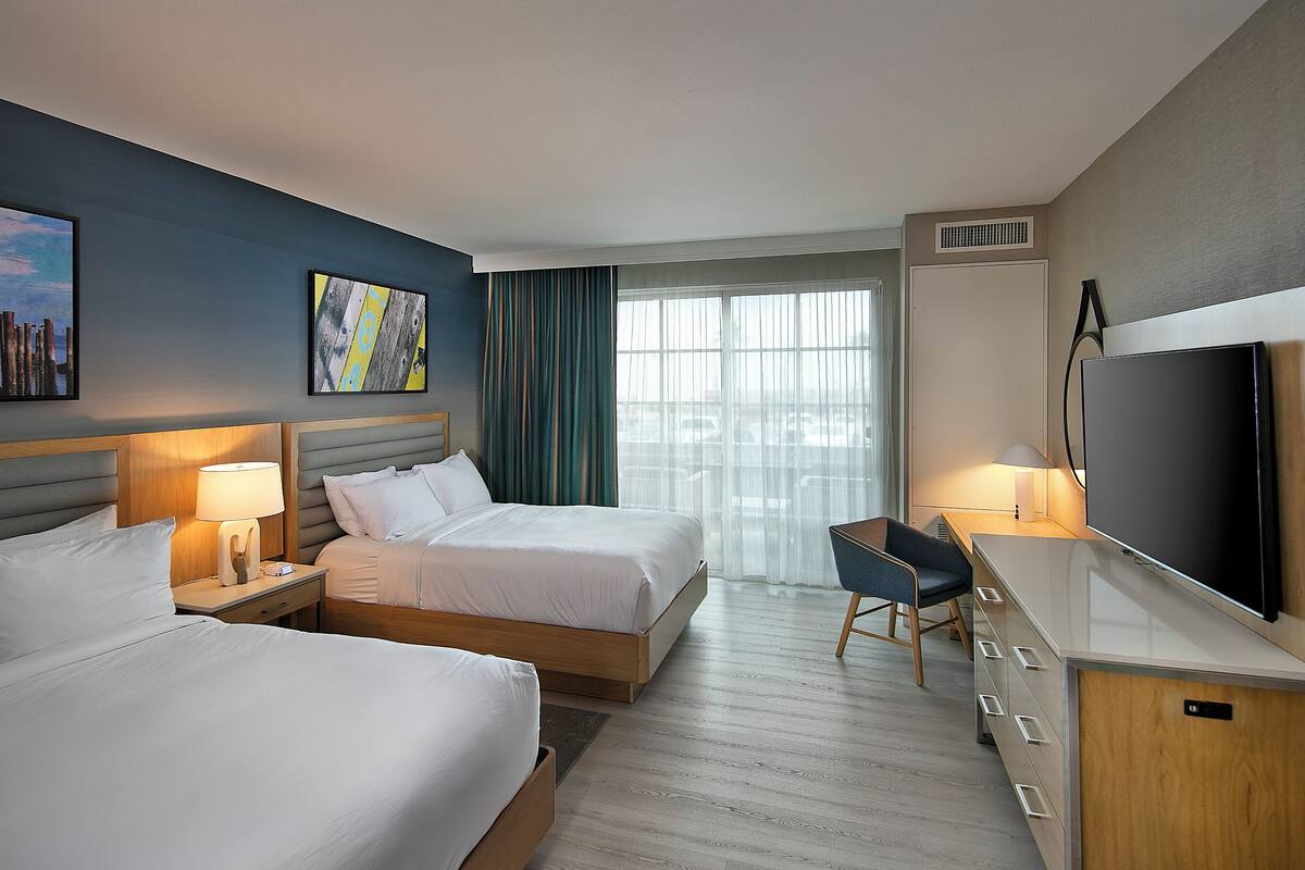 A hotel room with two beds, a desk, a TV, and a window with curtains.