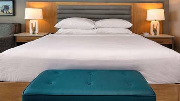 A neatly made bed with a teal bench in front, flanked by two bedside tables with lamps, in a room with a dark ceiling and framed pictures on the wall.