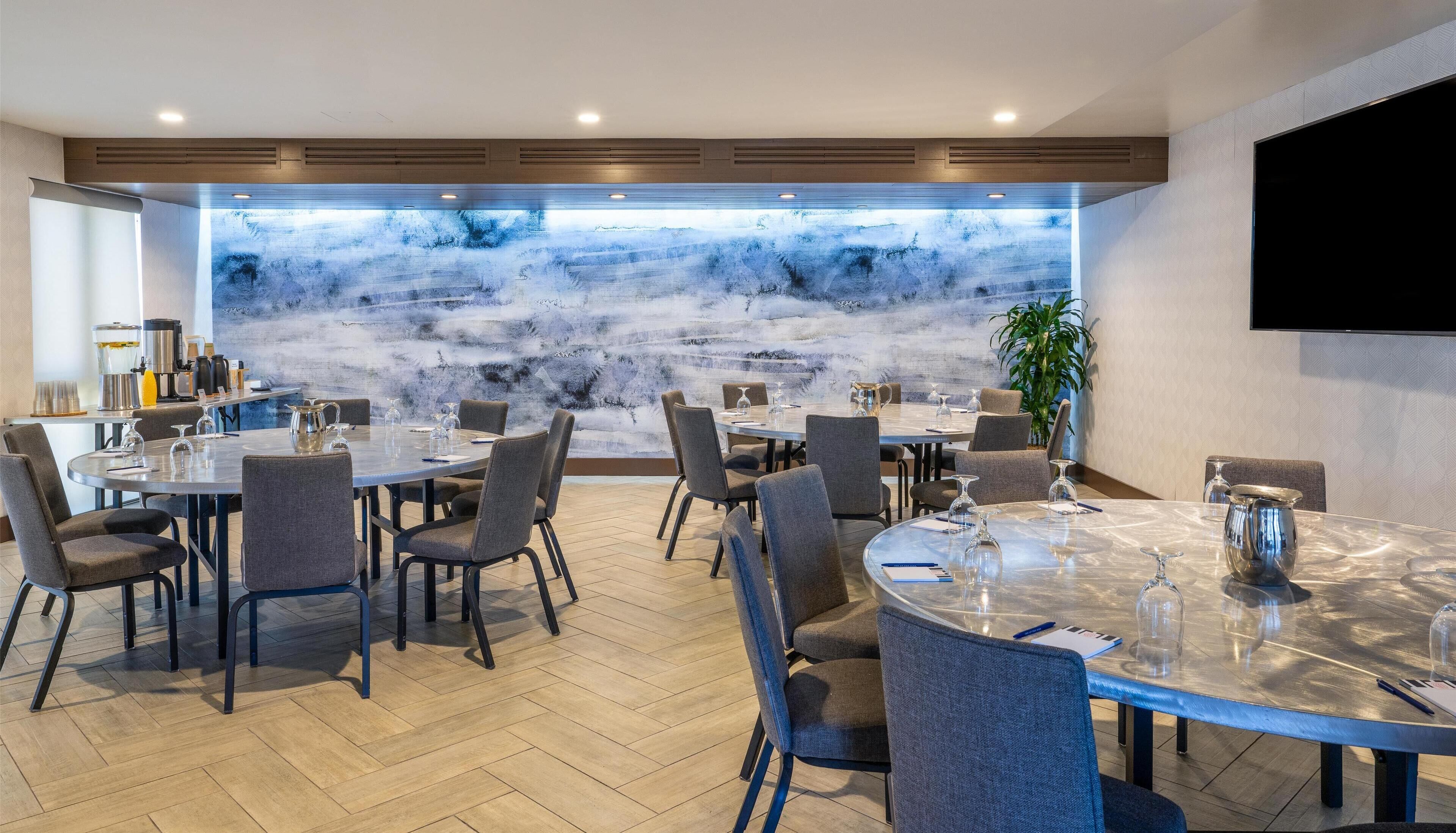A modern dining area with round tables, grey upholstered chairs, and a large window with a view of a mountainous landscape.