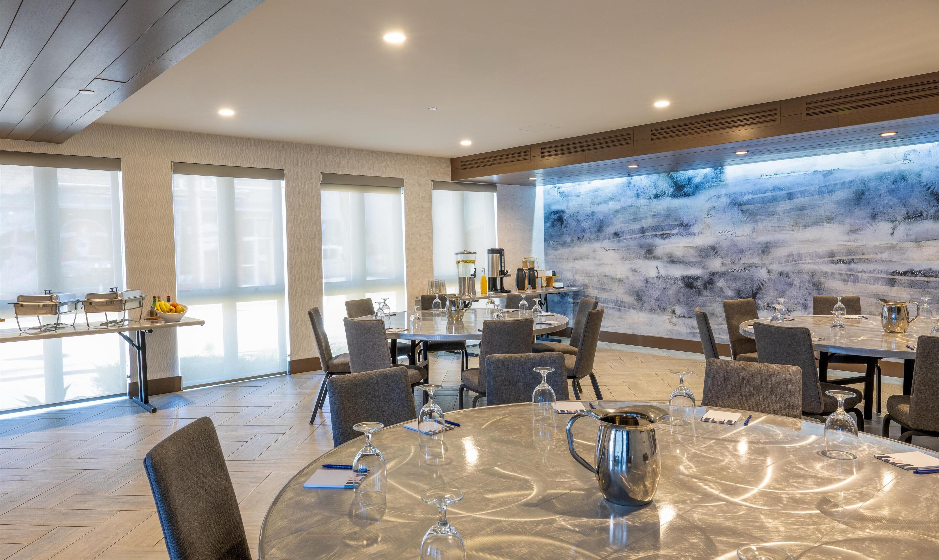 Un comedor moderno con mesas redondas, sillas y un ventanal con vistas a un paisaje montañoso.