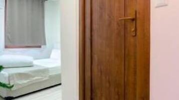 Una puerta de madera con un panel de vidrio, una cama con colchón blanco y manta gris, y piso de madera.