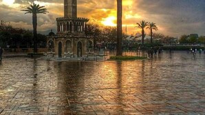 A historic tower with a clock, surrounded by palm trees and a paved square. - Agora Park Hotel (Izmir)
