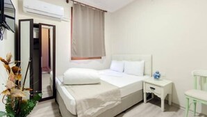 A hotel room with a bed, bedside table, chair, and an air conditioning unit. - Agora Park Hotel (Izmir)