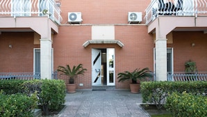 A building entrance with a brick facade, two potted plants, and a patterned walkway. - Hibiscus (Taranto)