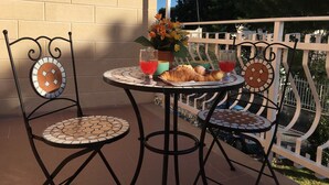 A patio with two chairs and a table, a flower vase, and a plate with croissants and a glass of red drink. - Hibiscus (Taranto)